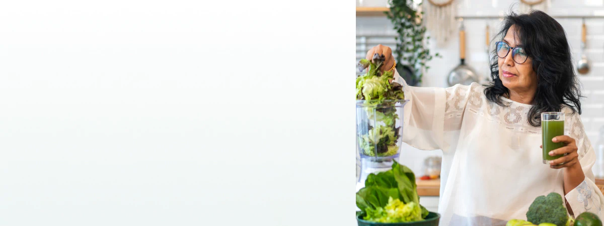 A woman in a kitchen blending leafy greens while holding a green juice, representing the benefits of supplements for cleanse and detox.